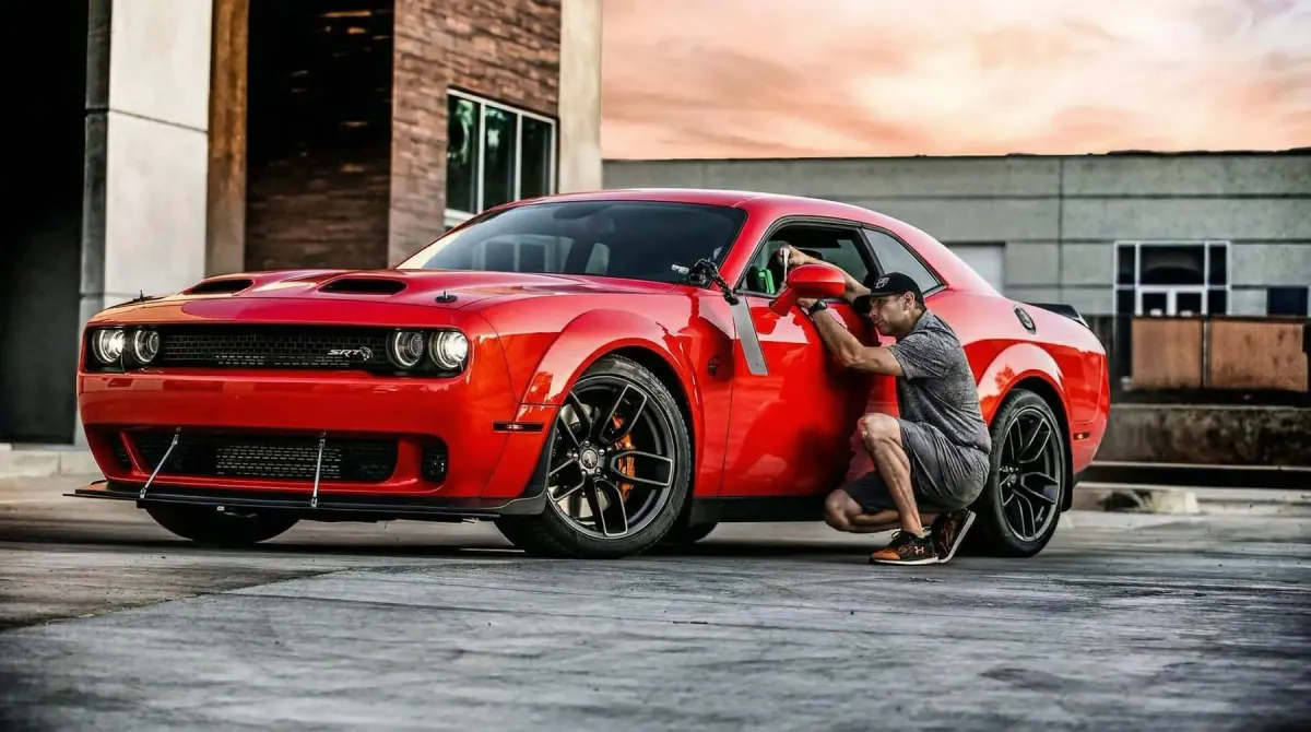 A Dent Time technician repairing a door dent on a red Dodge Challenger where it is parked