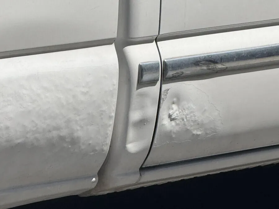 Body filler bubbling and splitting along a door edge months after a repair sold as paintless