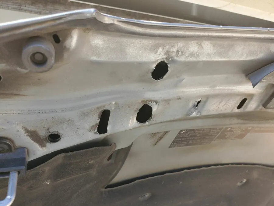 Holes drilled straight through a BMW hood and left unsealed during a bad dent repair