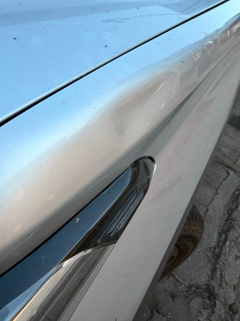 A shallow body line dent on a silver fender, photographed by the owner before any repair attempt