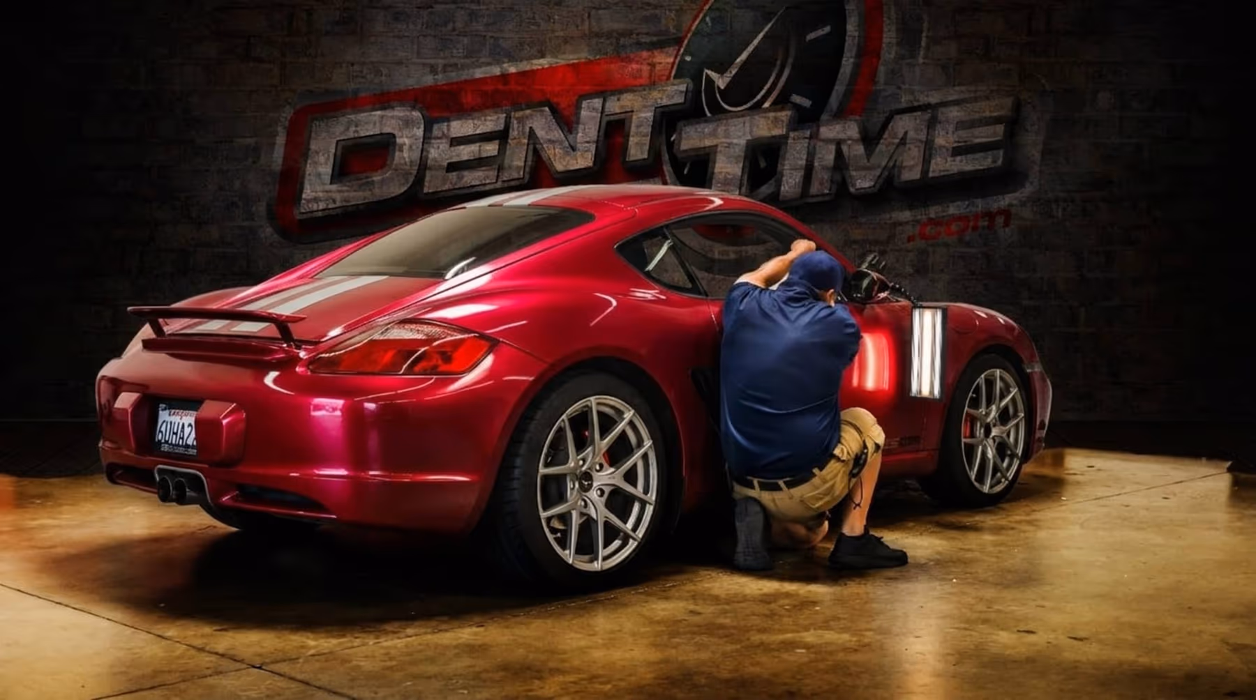 Myke Toledo reading a dent under a light board on a blue Porsche Cayman in a parking garage