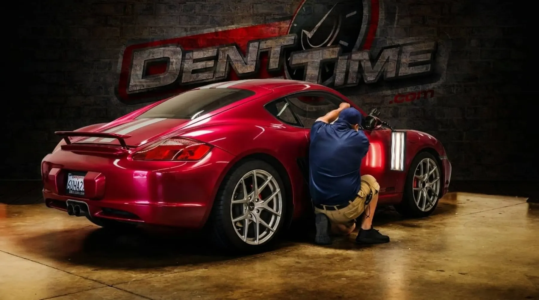 Myke Toledo reading a dent under a light board on a blue Porsche Cayman in a parking garage