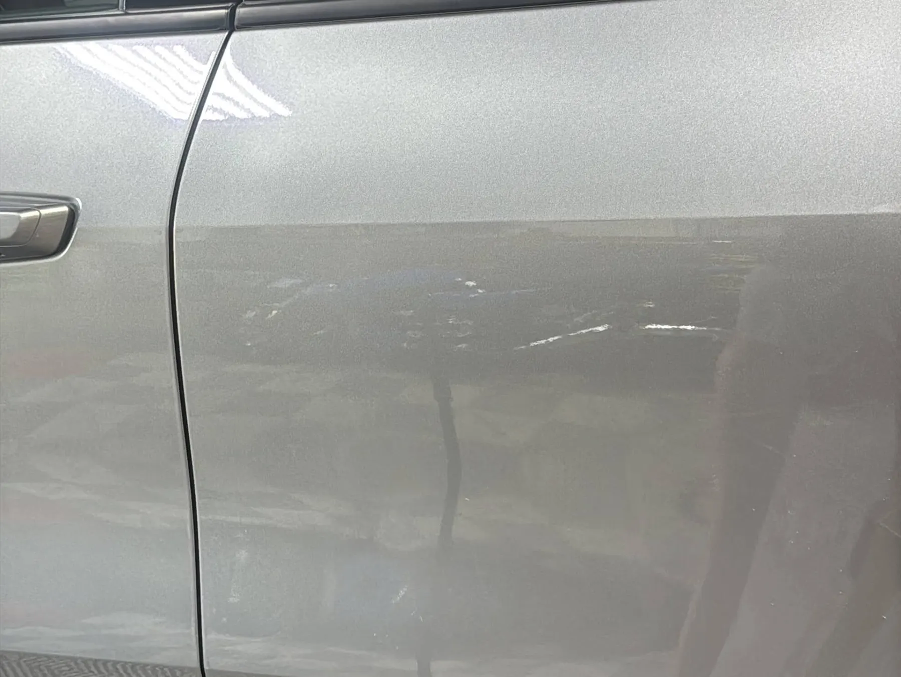 A silver car door after paintless dent repair, the reflection running straight across the panel