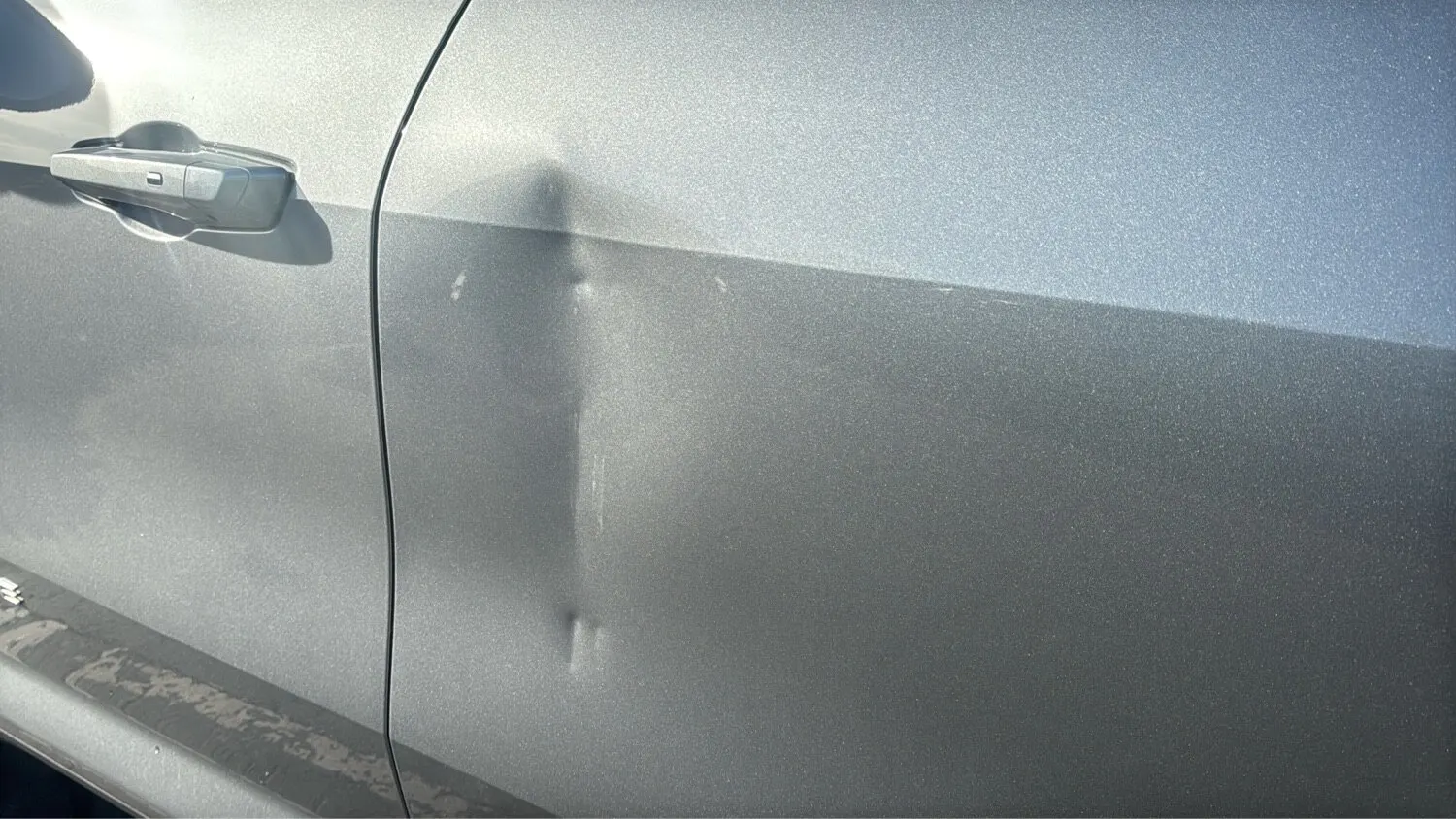 The same silver car door before repair, with the dent visible in the reflection