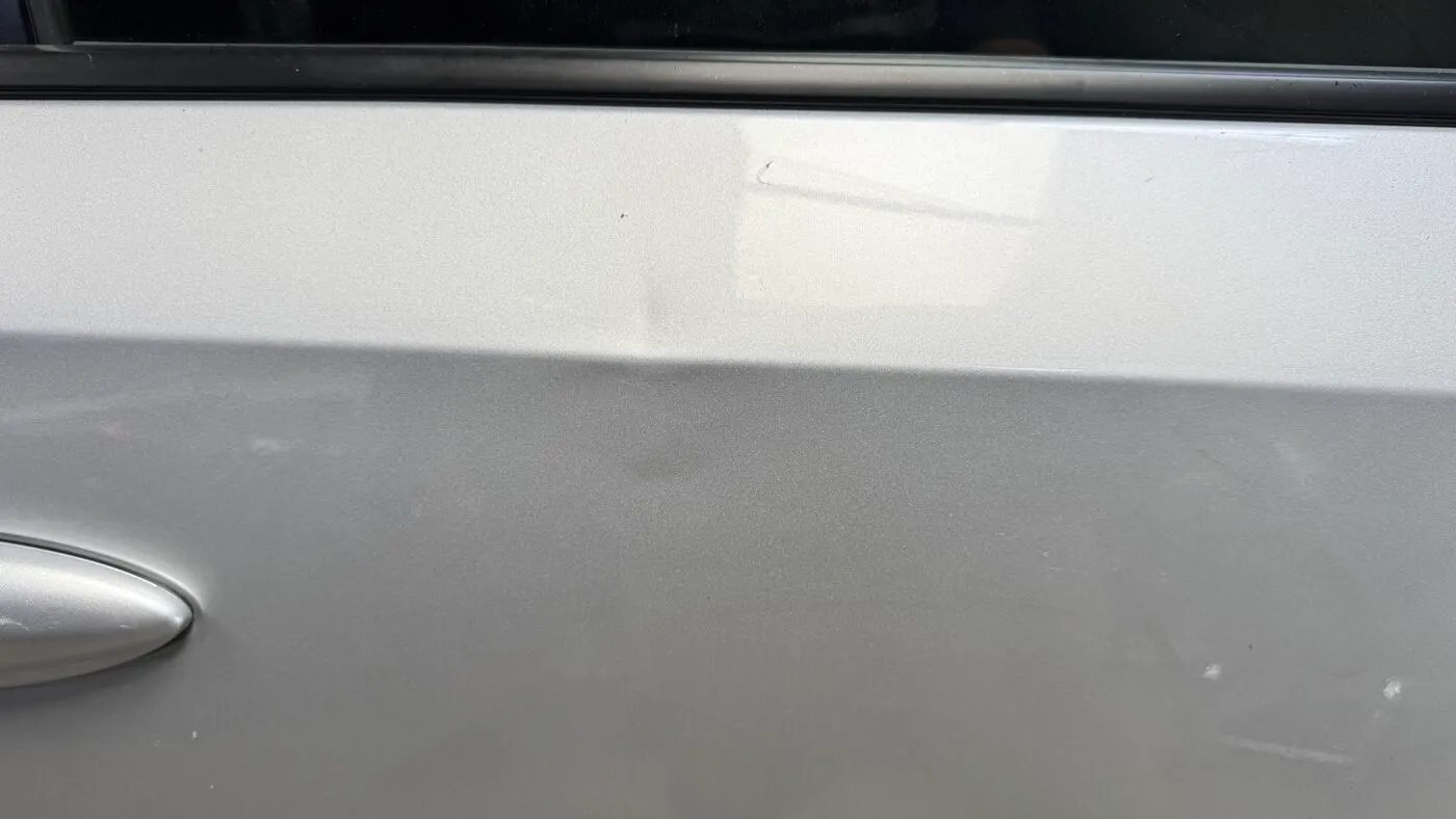 Silver door panel after an Improvement level paintless dent repair, damage substantially reduced
