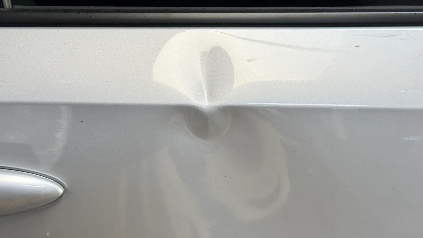 The same door panel before any repair, showing the full dent and crease